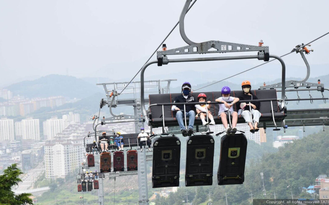 Ropeway Transport for Tourism showing families enjoying a chairlift ride above a scenic mountain city with beautiful hillside views